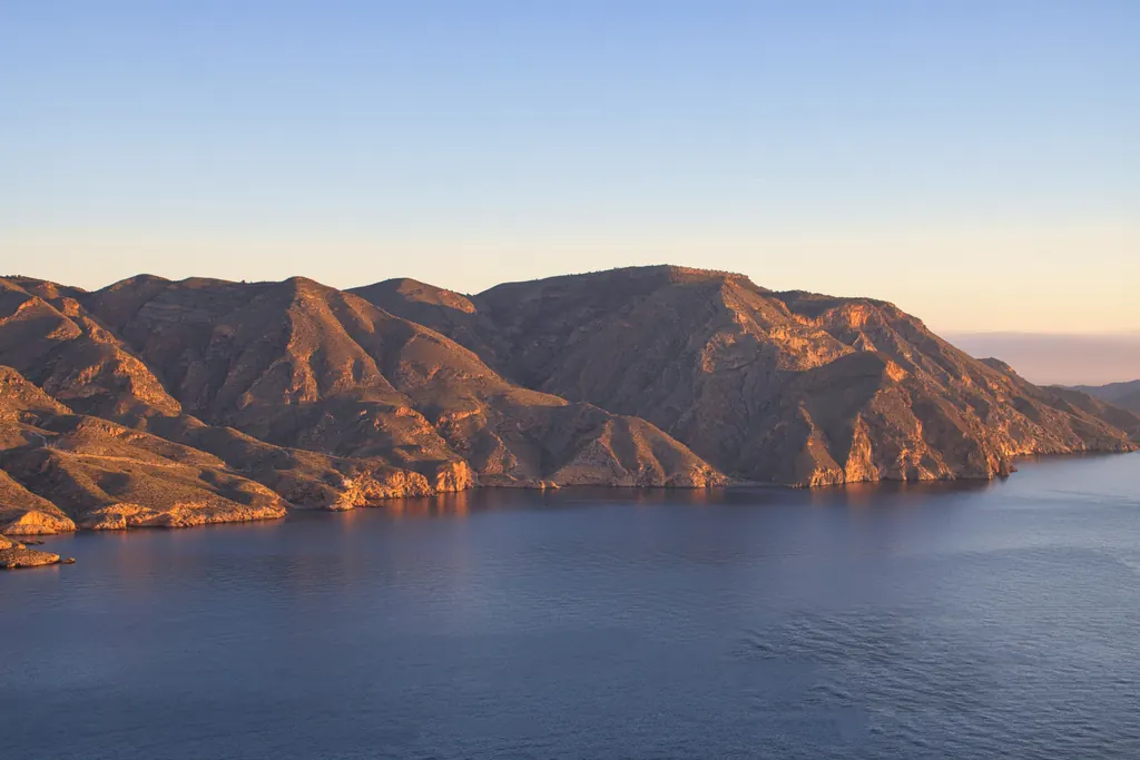 Low sun warming a rugged mountain coast in Spain above a calm blue sea, under a clear sky