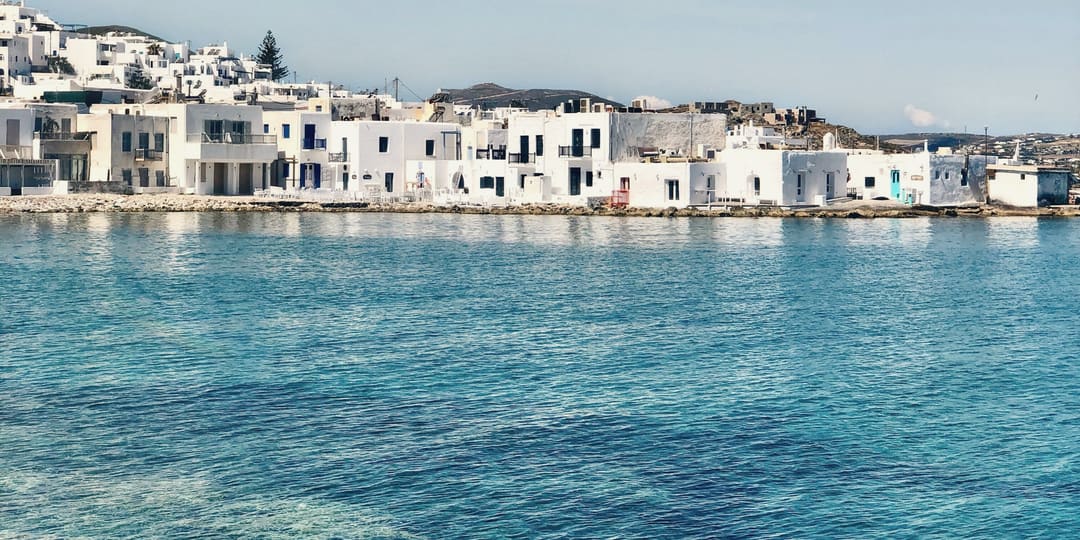 Whitewashed houses on a sunlit island waterfront, across clear turquoise water